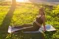 Peaceful young positive pregnant woman in gymnastic suit does yoga and meditate sitting on mat on green grass on sunny Royalty Free Stock Photo