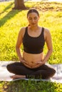 Peaceful young positive pregnant woman in gymnastic suit does yoga and meditate sitting on mat on green grass on sunny Royalty Free Stock Photo