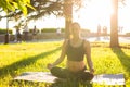 Peaceful young positive pregnant woman in gymnastic suit does yoga and meditate sitting on mat on green grass on sunny Royalty Free Stock Photo