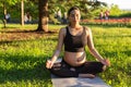 Peaceful young positive pregnant woman in gymnastic suit does yoga and meditate sitting on mat on green grass on sunny Royalty Free Stock Photo