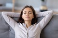 Peaceful young woman with hands behind head relaxing at home