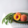 Peach in halves with bone in minimalistic style. Peaches with leaves on color green plate on table with white tablecloth. Ripe Royalty Free Stock Photo