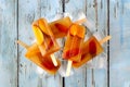 Peach iced tea popsicles with ice on rustic blue wood