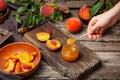 Peach jam in glass jar on wooden table. Spoon of Peach jam in female hand. Canned fruit jam, peach wedges and whole fruit. .