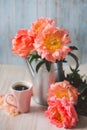 Peach peony bouquet in a metal watering can with hot coffee in pink cup on a blue background Royalty Free Stock Photo