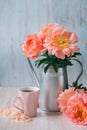 Peach peony bouquet in a metal watering can with hot coffee in pink cup on a blue background Royalty Free Stock Photo