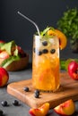 Peach tea with ice, mint and blueberry on tall glass. Vegan homemade cold healthy drink on a wooden board on a dark background