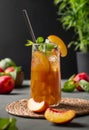 Peach tea with ice and mint on tall glass. Vegan homemade cold summer drink on a dark background with fresh fruits.