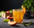 Peach tea with ice and rosemary on a glass. Vegan homemade healthy drink on a dark background with fresh fruits close up. Rustic