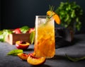 Peach tea with ice and rosemary on a tall glass. Vegan homemade healthy drink on a dark background with fresh fruits close up.