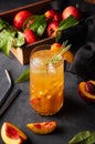 Peach tea with ice and rosemary on a tall glass. Vegan homemade healthy drink on a dark background with fresh fruits