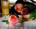 Peaches on a branch with leaves in a wicker from rods bowl and a glass of peach juice on a light wooden background