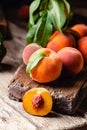 Peaches with leaves on dark wooden board with peach in halves with peach seed stone. Composition with ripe juicy peaches Harvest