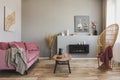 Peacock chair with blanket in grey living room interior with pastel pink couch and coffee table