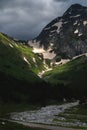 peak of the mountain in snow and clouds, at the foot of the lush green grass and a mountain river. large plan, summer Royalty Free Stock Photo