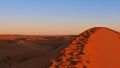 Peak of orange colored sand dune in the evening with footprints in the desert of Erg Chebbi near Merzouga, Morocco, Africa. Royalty Free Stock Photo
