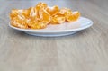 Pealed mandarin peaces on white plate, wooden desk surface