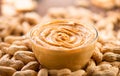 Peanut butter in a glass bow over raw peanuts background. Creamy smooth peanut butter in glass bowl