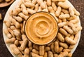 Peanut butter in a glass bowl over raw peanuts background. Creamy smooth peanut butter in glass bowl