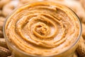 Peanut butter swirls in a glass bowl over raw peanuts background. Creamy smooth peanut butter in jar Royalty Free Stock Photo