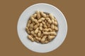 Peanuts on a white plate, isolated on brownbackground