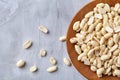 Peanuts in wooden plate over white textured background, top view, close-up.