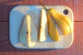 Pear cuted into slices on a wooden board onred-brown table with a long blue shadow