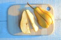 Pear cuted into slices on a wooden board on turquoise table with a long blue shadow