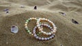 Pearl multicolored iridescent bracelets lie on the yellow sand dune with purple shells next to the sea.