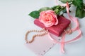 Pearl necklace on rose velvet box and pink one rose with gift card. Light background