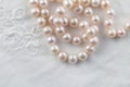Pearl necklace on white embroidered linen background - top view of string of pink pearls Royalty Free Stock Photo