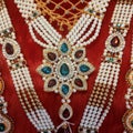 Pearls and colourful stones golden necklace on red velvet background