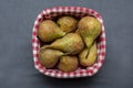 Pears lie in a wicker wooden basket on a dark background, close-up, top view, checkered fabric.