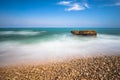 Pebble beach and silk effect in the Mediterranean Sea, rocks and foam with blue sky and clouds