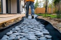 Pebble path installation in garden with geotextile borders as worker steps along new walkway beside deck Royalty Free Stock Photo