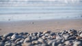 Pebble rocks, sandy beach, ocean sea water waves, round smooth stones or boulder