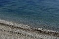 Pebble sea shore with azure clear water. Traces from the car leveling the surface of the beach. Diagonal background