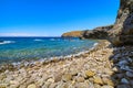 Pebble stone beach and high cliffs on sunny summer day. Clear blue sky, sunshine, azure clear sea waters, Milos island Royalty Free Stock Photo