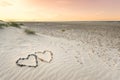 Pebbles arranged in shape of two hearts on sand beach ripples with beautiful sunset. Royalty Free Stock Photo