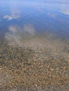 Pebbles at the bottom of a clear lake. The sky with clouds is reflected in the water Royalty Free Stock Photo