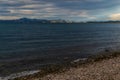 Pebbles shore of blue Lake Baikal, mountains on the horizon in sunset light, clouds. Evening