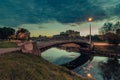 a pedestrian concrete bridge with metal handrails over a narrow river in the autumn evening city park is illuminated by the light Royalty Free Stock Photo