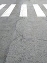 Pedestrian crossing on cracked asphalt. White lines marking background on the ground. Zebra crossing on a road close up. Crosswalk Royalty Free Stock Photo