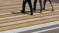 Pedestrian crossing on the stone road. White and yellow stripes on which three men pass in sneakers. Legs of people in jeans. The Royalty Free Stock Photo