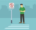 Pedestrian safety. Isolated man standing beside `No phones` sign while using mobile phone.