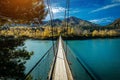 Pedestrian suspended wooden bridge over mountain river. Long bridge across the river against background of mountains covered with Royalty Free Stock Photo
