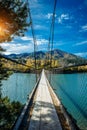 Pedestrian suspended wooden bridge over mountain river. Long bridge across the river against background of mountains covered with Royalty Free Stock Photo