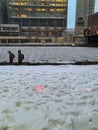 Pedestrians bundled up against the cold and snow walk alongside the frozen Chicago River