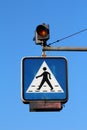 Pedestrians crossing blue and white road sign suspended from metal pole with two blinking yellow lights mounted on top