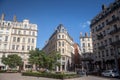 Pedestrians walking on Place des Jacobins in Lyon, France, facing a Haussmann style building and some commercial shop and stores